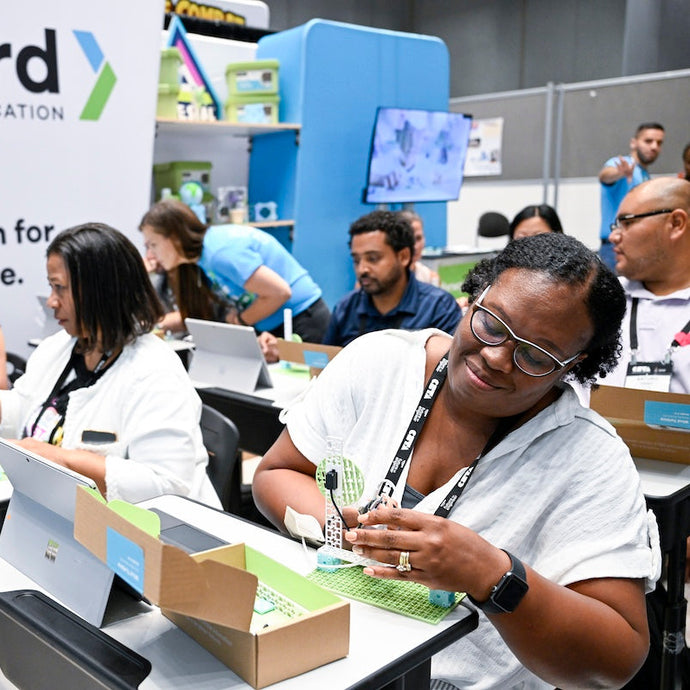 Teacher exploring STEM education kit at conference booth with laptop and product demo | Forward Education