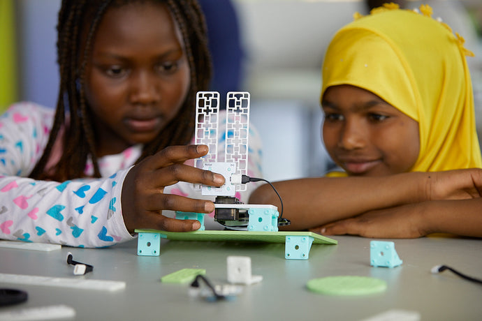 Two students assembling a green circuit board with white keyboard and turquoise connectors | Forward Education