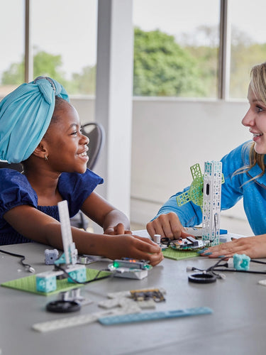 Educator demonstrating wind turbine STEM kit to three students at table | Forward Education