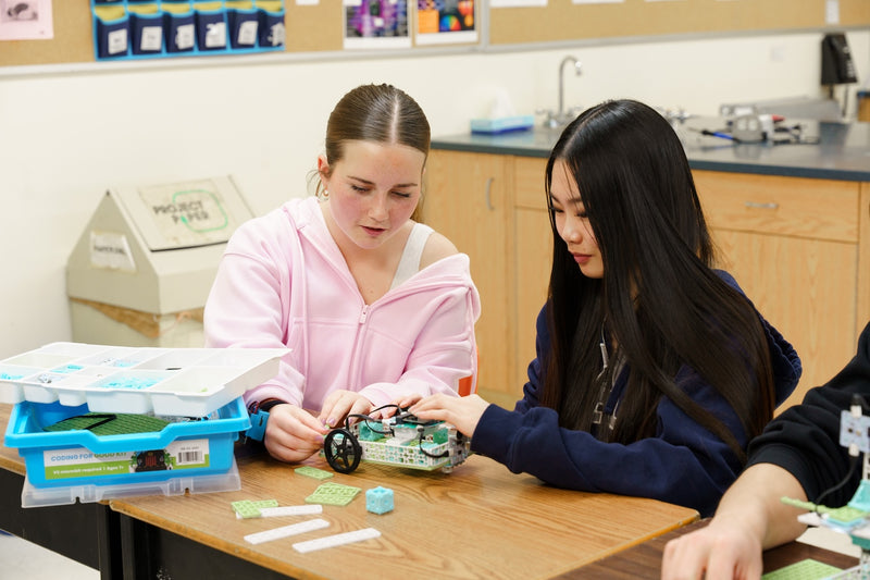 Students assembling a small robotic vehicle with green circuit board and wheel components | Forward Education