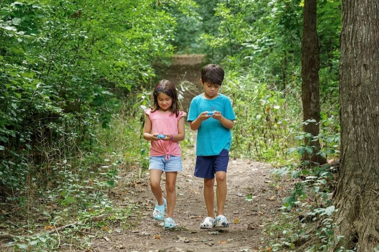 Two students walking in a forest holding the CHARGE for micro:bit device