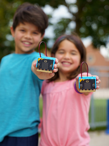 Two students holding the CHARGE for micro:bit devices smiling 