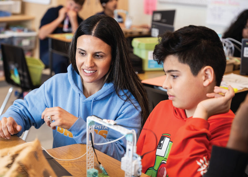 Teacher and student examining white robotics kit at wooden desk in classroom | Forward Education